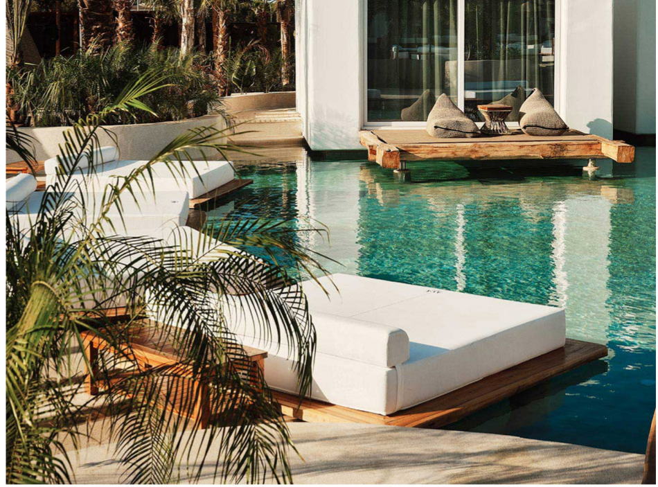 A daybed at the water’s edge among palms